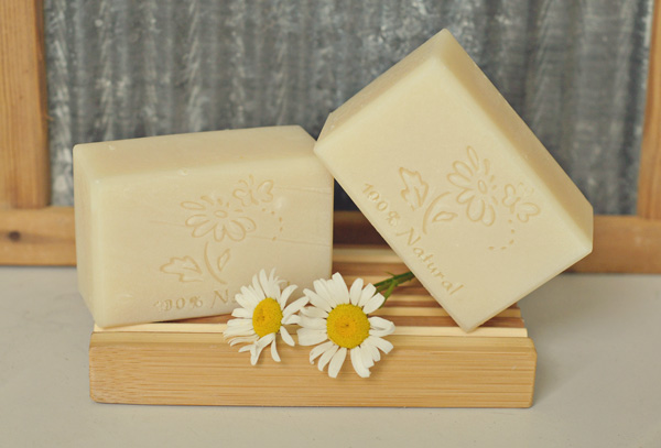 A picture of two fragrance free creamy bars of soap from Country Bubbles. They are on a dish with a daisy. 